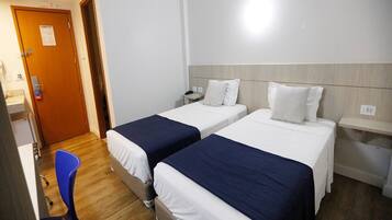 A hotel room with two single beds, a desk, a chair, and a wooden floor.