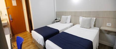 Habitación de hotel con dos camas individuales, un escritorio, una silla y suelo de madera.