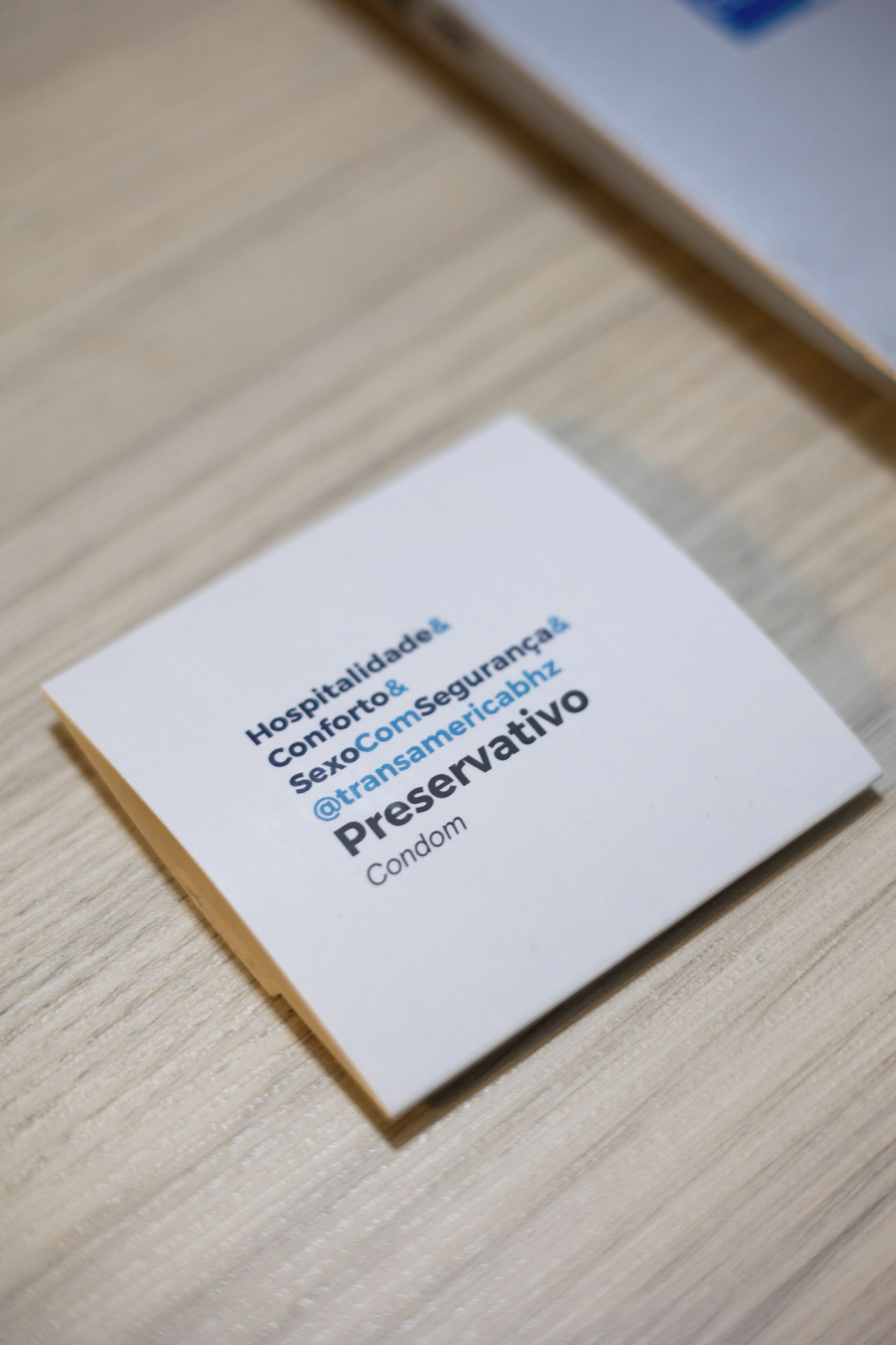 A white business card with text in Portuguese, placed on a wooden surface.
