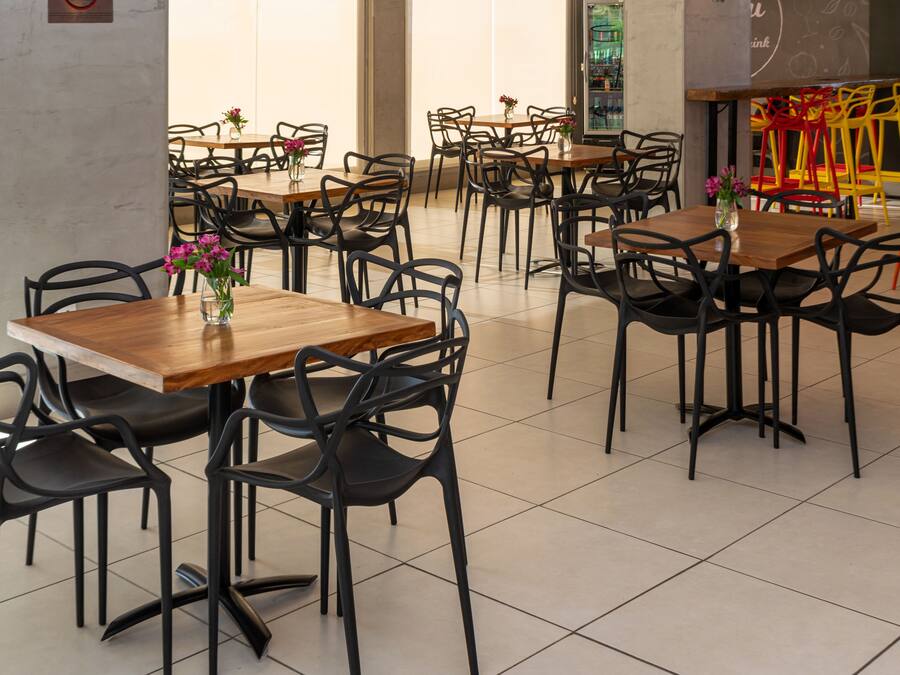 A modern restaurant with wooden tables and black chairs, featuring a green wall and a tiled floor.