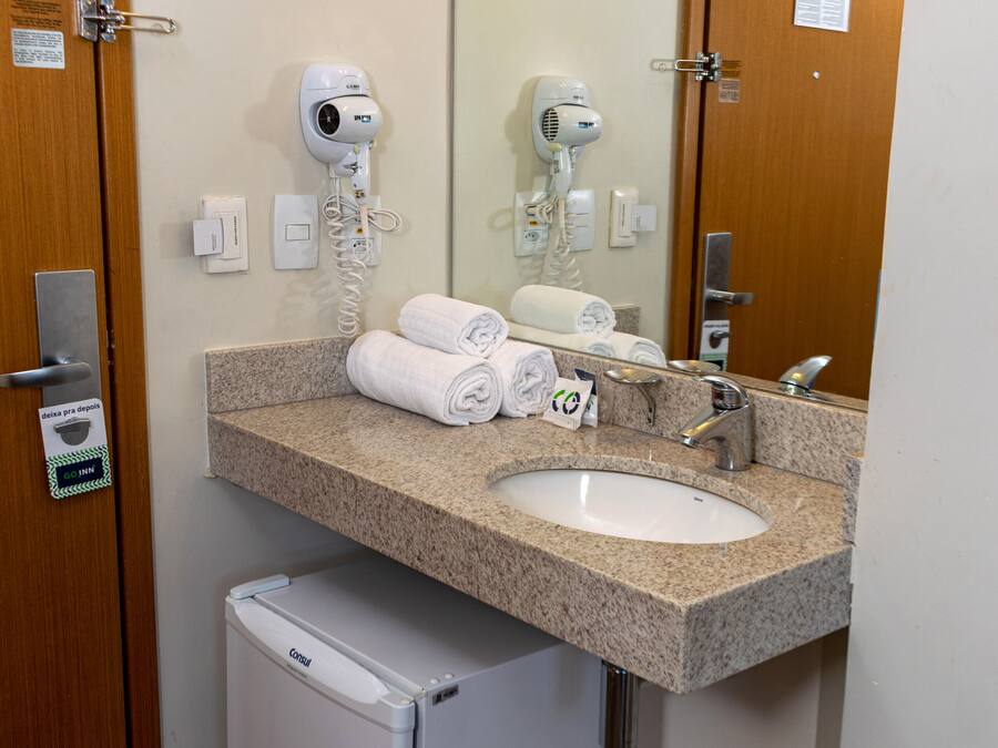 A bathroom with a sink, towel dispenser, hair dryer, and a small refrigerator.