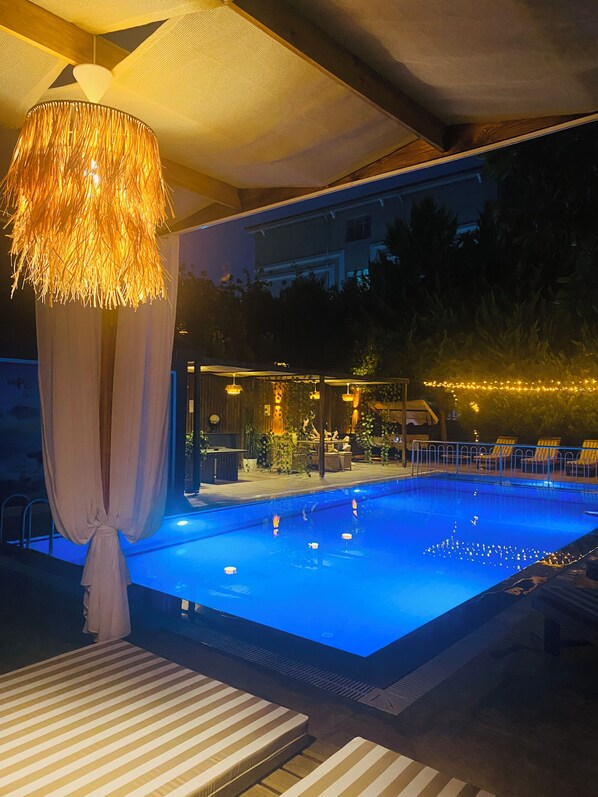 An indoor swimming pool with a canopy, lounge chairs, and a bar area.
