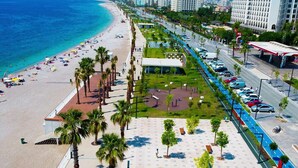 A beachside promenade with a parking area, palm trees, and a view of the ocean. - Royal Loft Suit (Konyaalti)