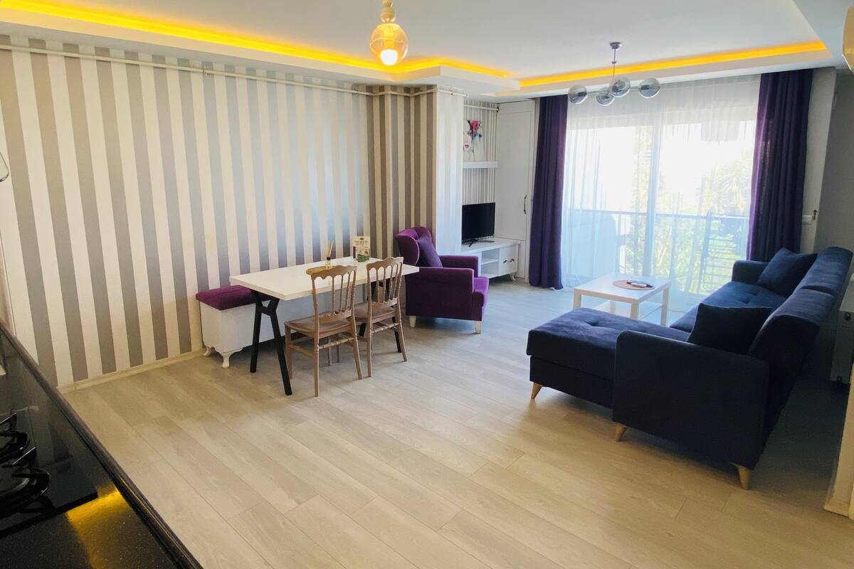 A modern living room with a dining area, a sofa, a TV, and a balcony with curtains.