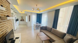 A modern living room with a sofa, a TV, and a dining area with chairs and a table. - Royal Loft Suit (Konyaalti)