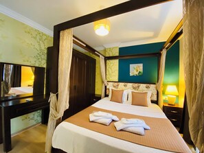 A four-poster bed with a headboard, a bedside table, a mirror, and a nightstand with a lamp.