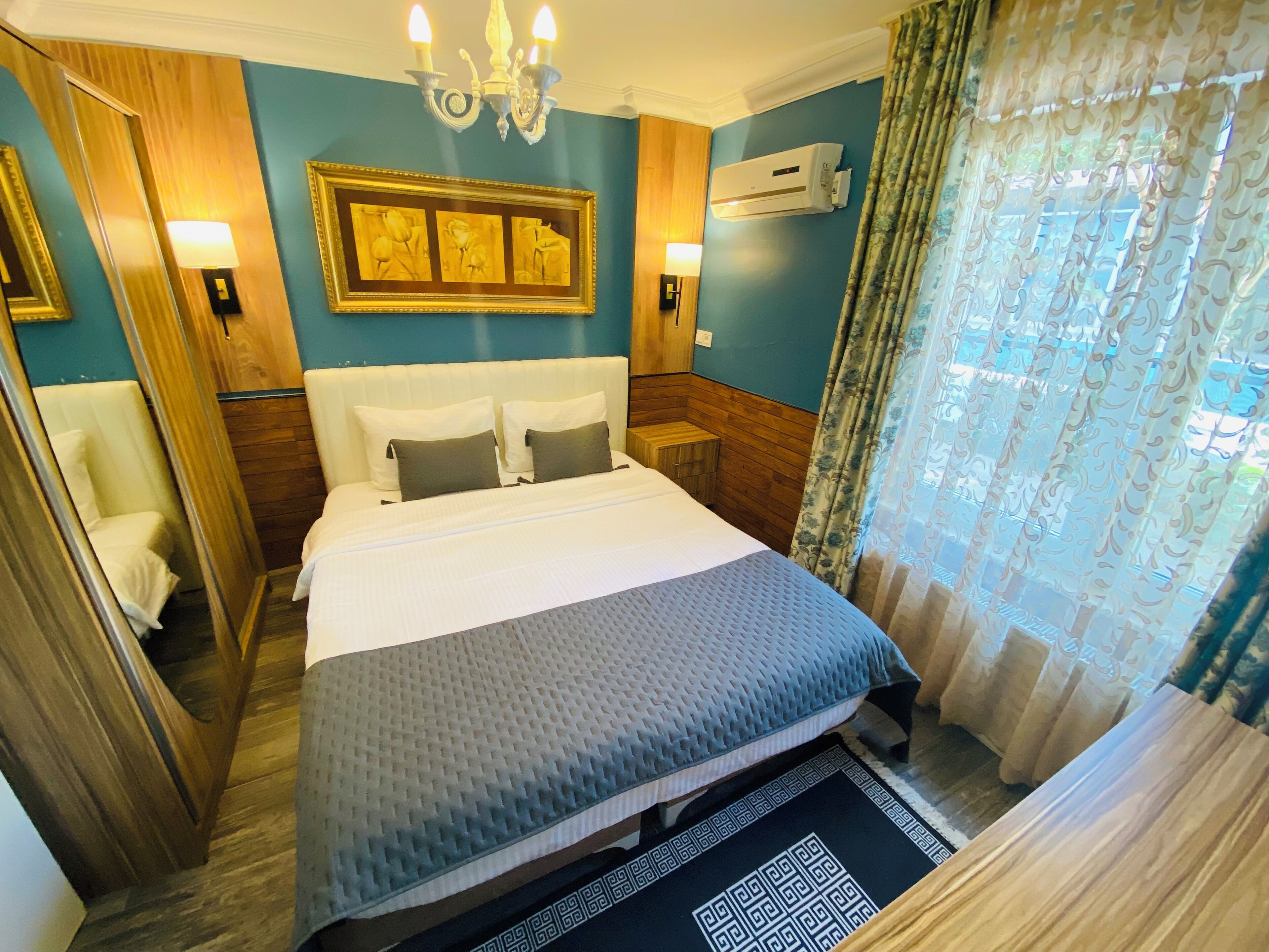 Une chambre d’hôtel avec un lit, un lustre, un climatiseur fixé au mur et un tableau encadré au-dessus du lit.