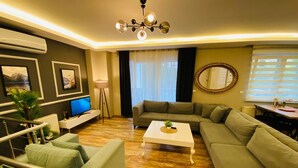 A modern living room with a sofa set, a coffee table, a TV, and a chandelier. - Royal Loft Suit (Konyaalti)