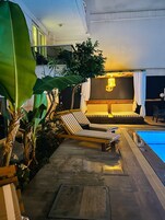 A poolside area with lounge chairs and a seating area with a patterned cushion.
