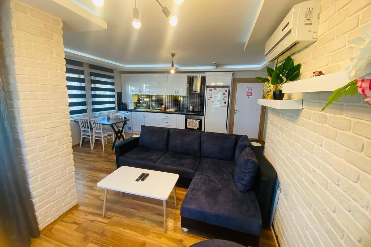 A modern living room with a sofa, a small table, and a kitchen in the background.