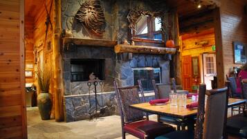 A rustic wooden interior with a stone fireplace, wooden dining table, and chairs.