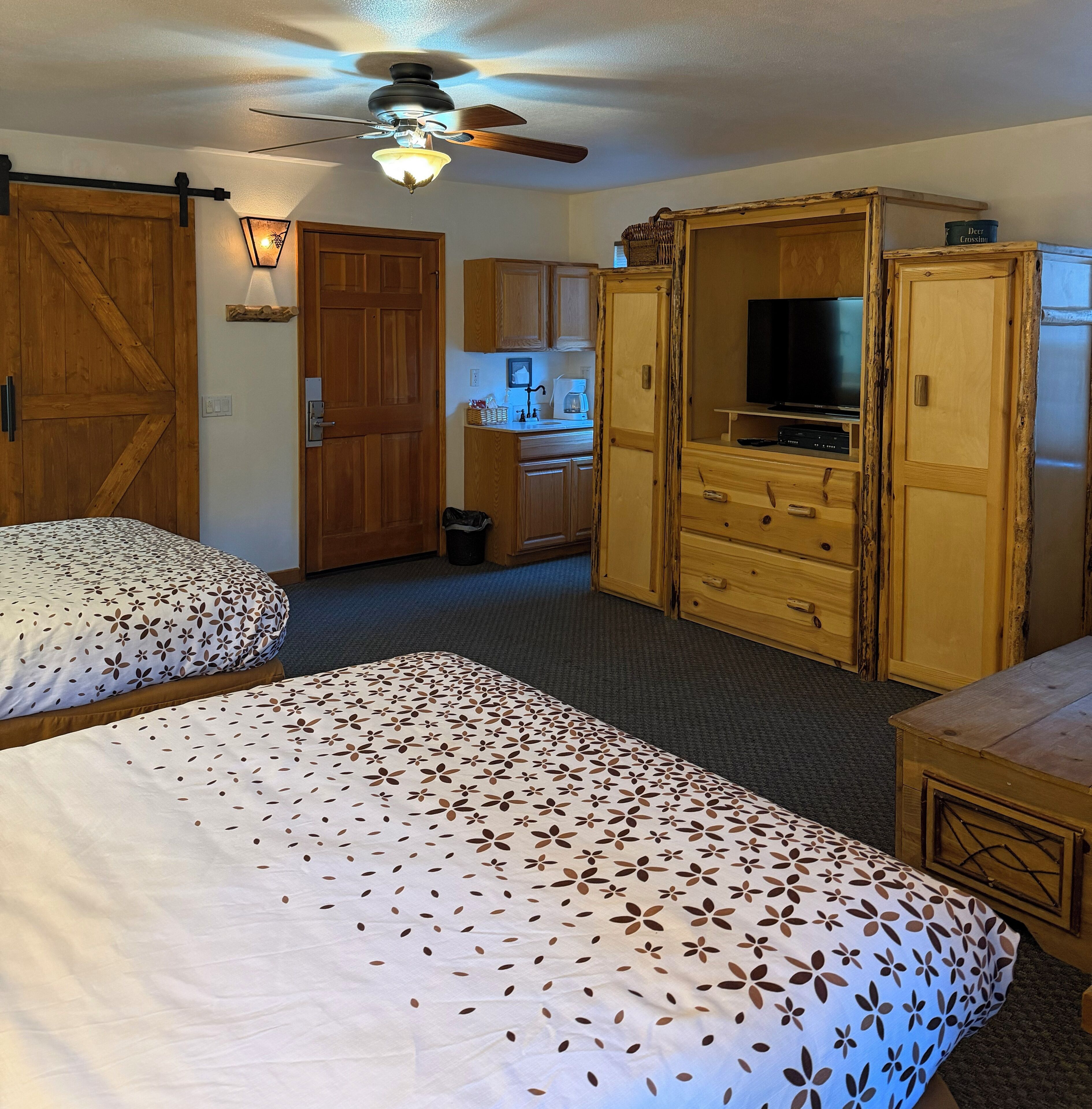 A room with two beds, wooden cabinets, a television, and a ceiling fan.