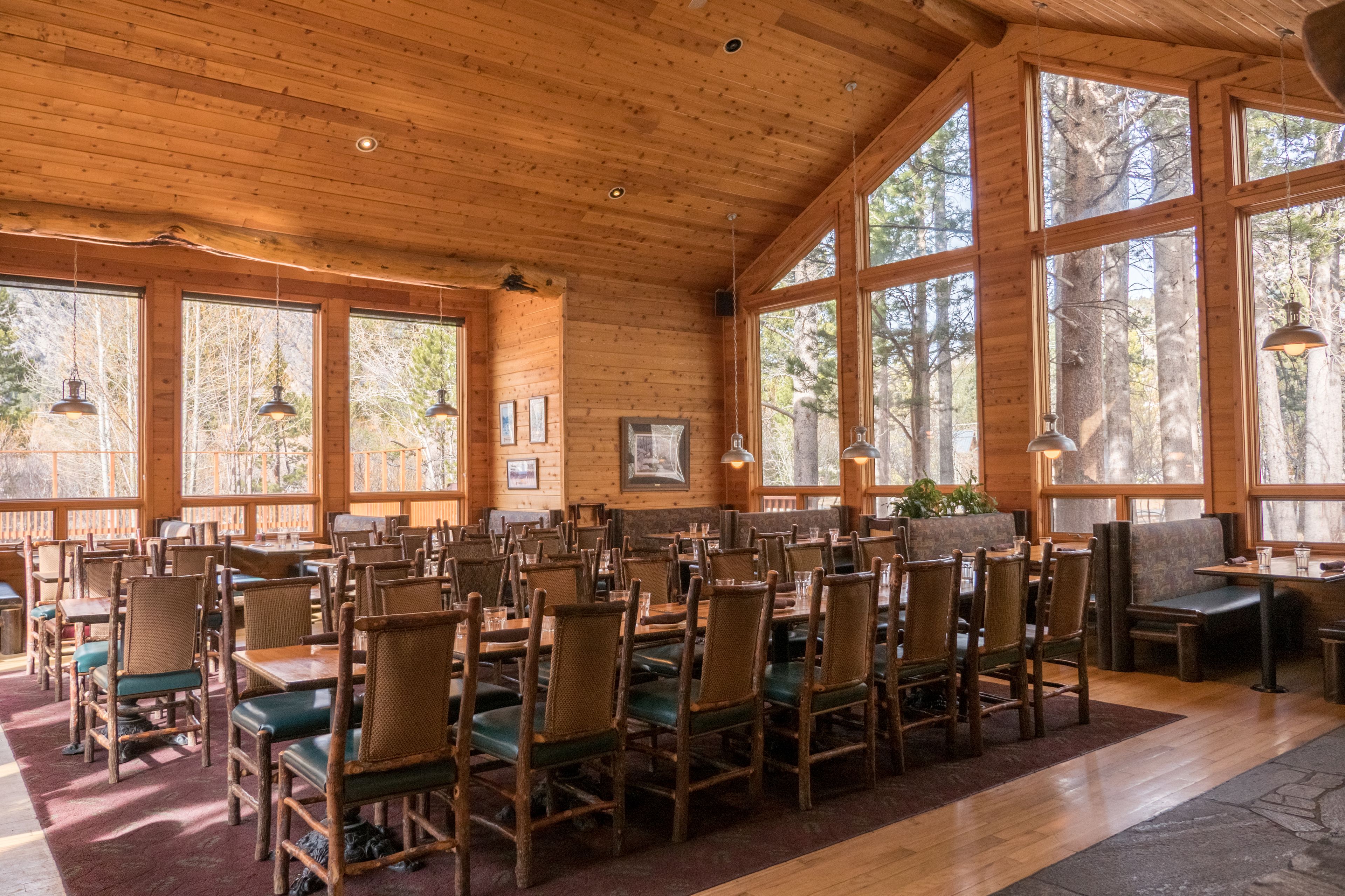 A spacious dining area with wooden tables and chairs, large windows, and hanging pendant lights.