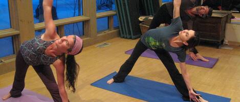 A yoga class in a room with large windows, wooden floors, and exercise balls in the background.