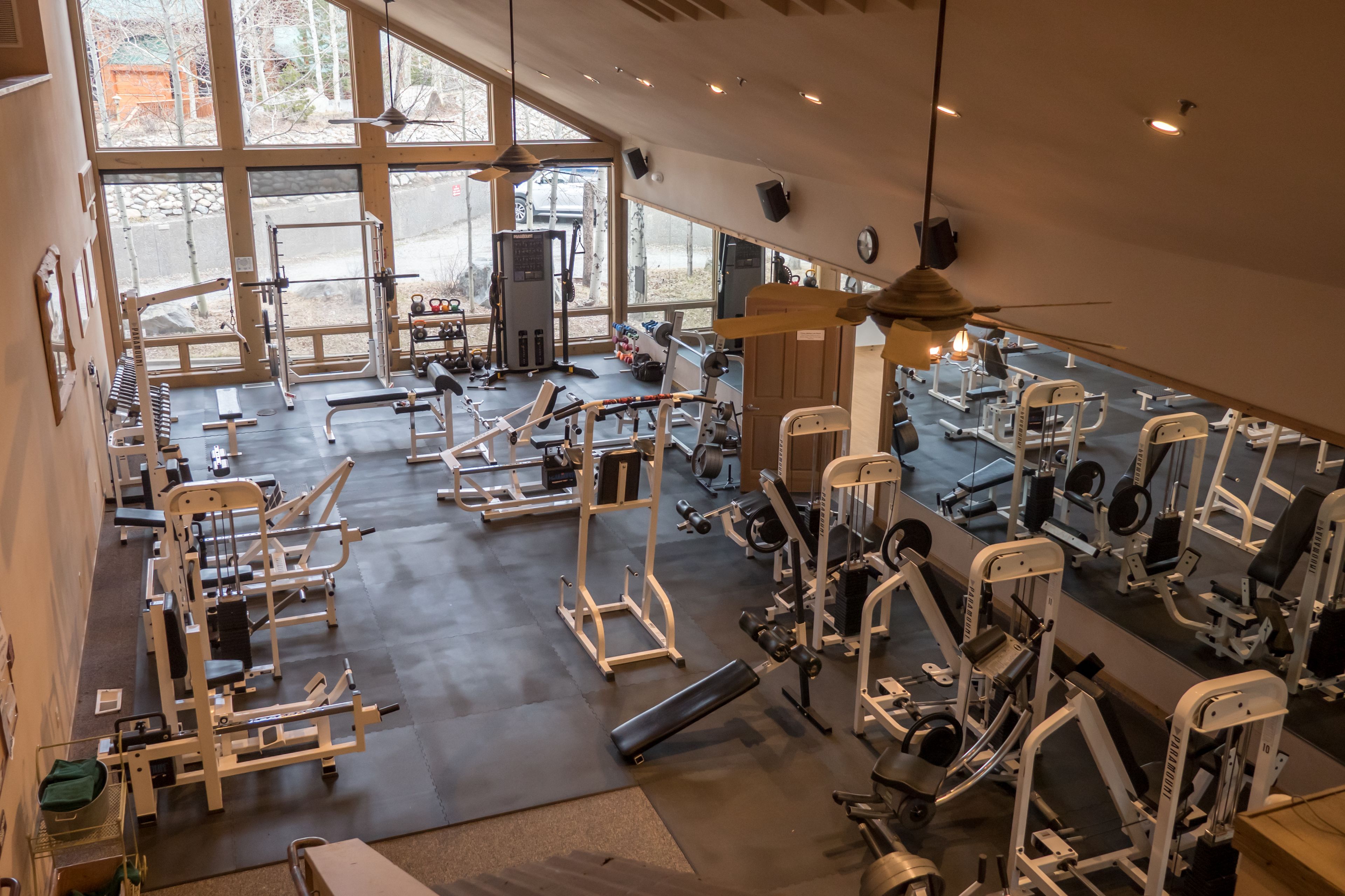 A gym with various exercise machines, large windows, and a high ceiling.