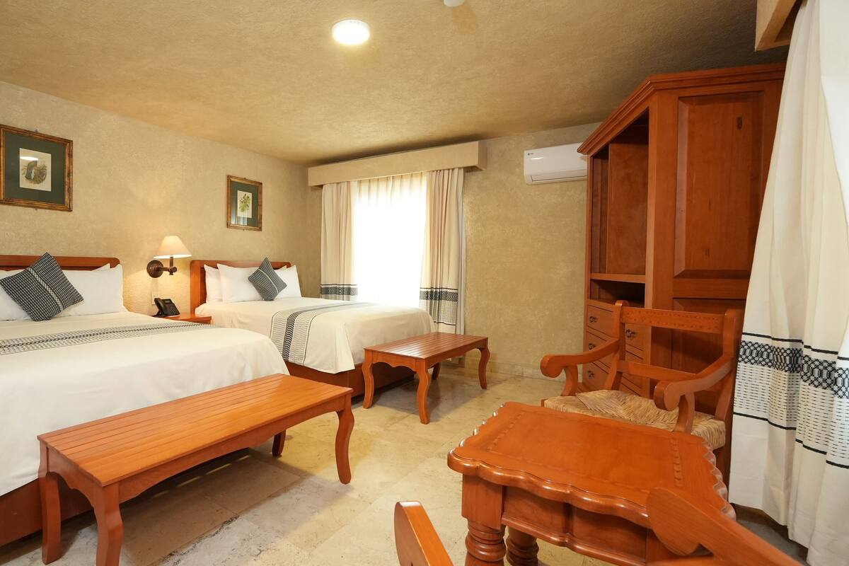 Habitación de hotel con dos camas, un banco de madera, una mesa de madera y un armario.