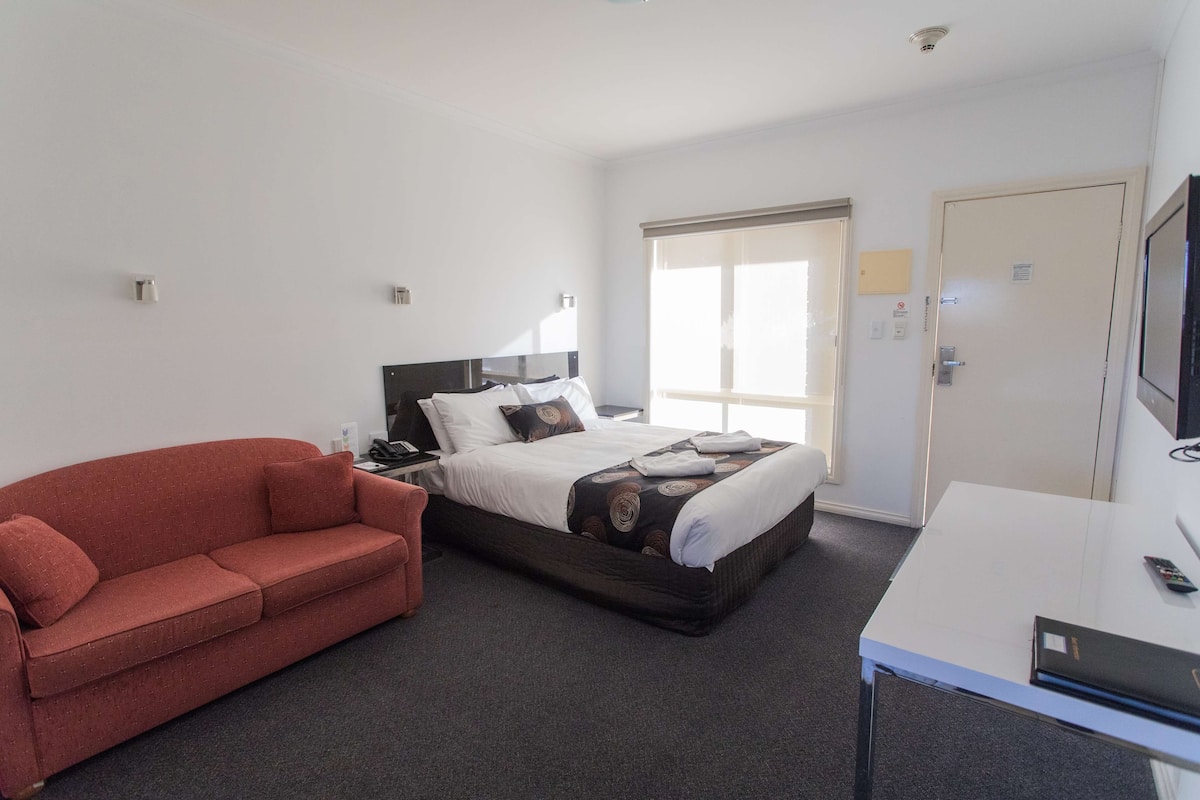 Una habitación de hotel con una cama, un sofá rojo, un escritorio y un televisor.