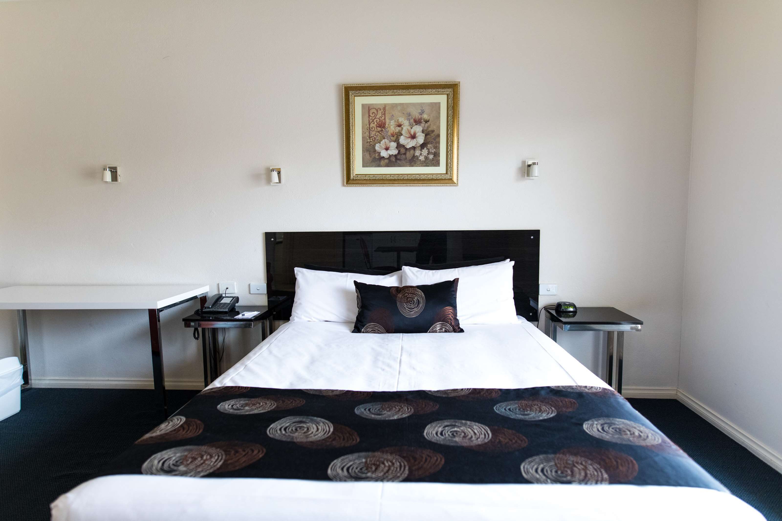 Una habitación de hotel con una cama grande, una mesita de noche con una lámpara y un cuadro colgado en la pared.