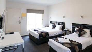 A hotel room with two beds, a desk, a TV, and a window with a view.