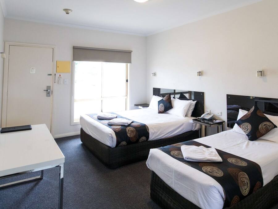 A hotel room with two beds, a desk, a TV, and a window with a view.