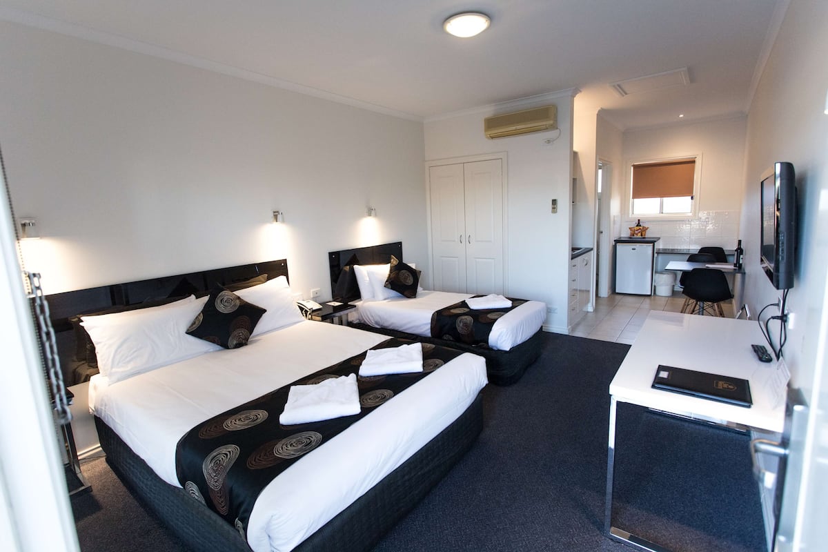 Habitación de hotel con dos camas, un escritorio, televisor y kitchenette.