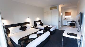 A hotel room with two beds, a desk, a television, and a kitchenette.