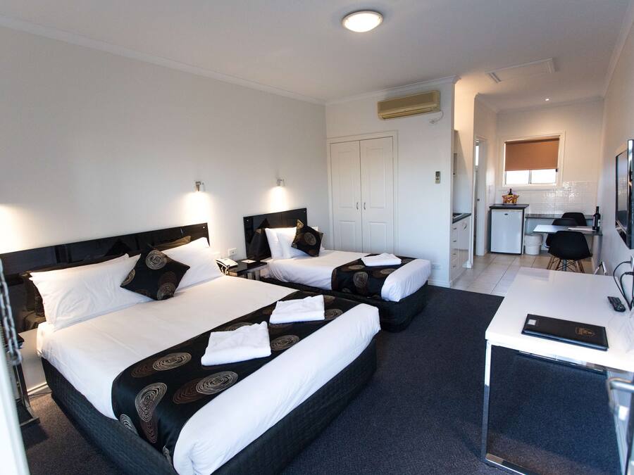 A hotel room with two beds, a desk, a television, and a kitchenette.