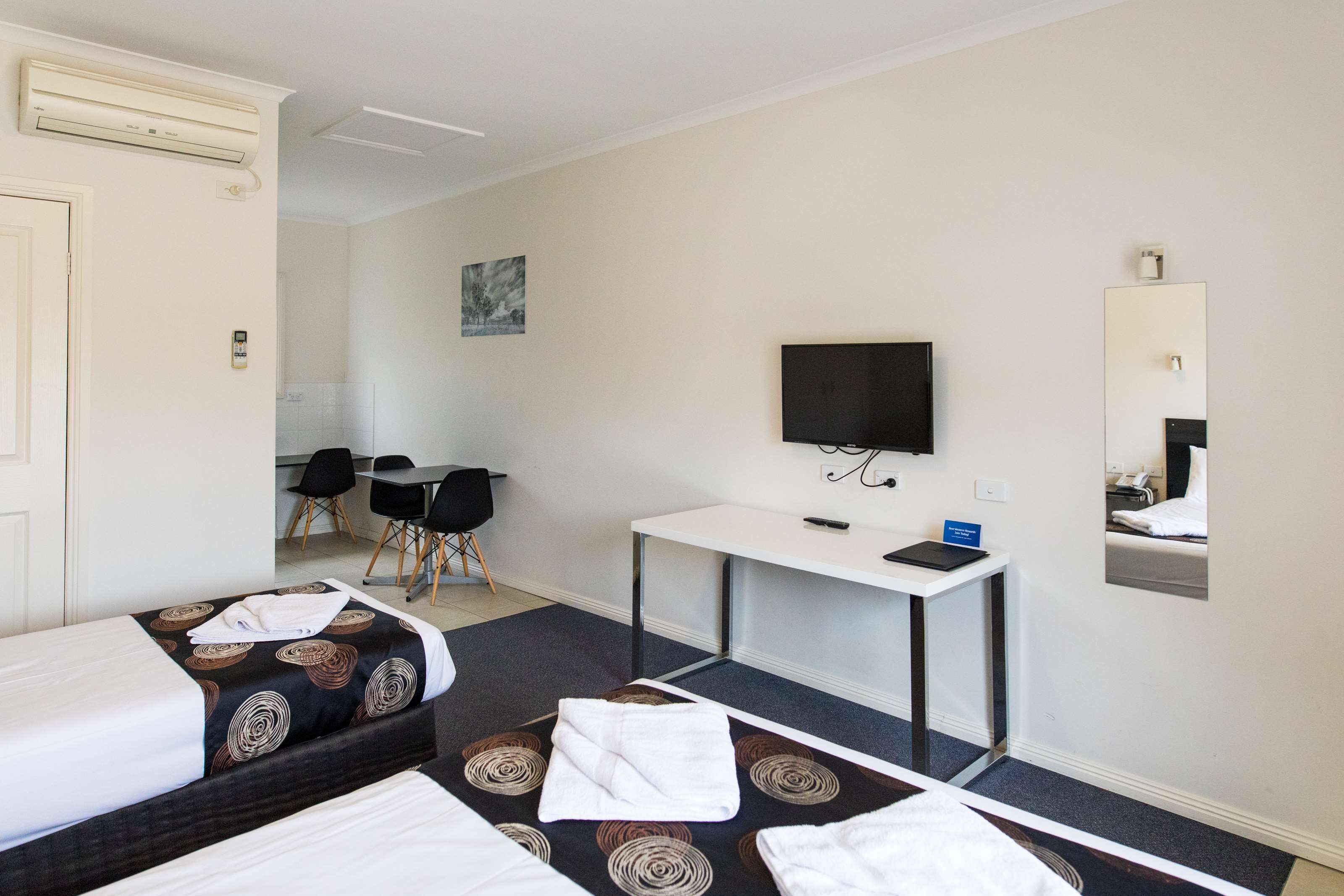 A hotel room with two beds, a desk, a TV, and a mirror.