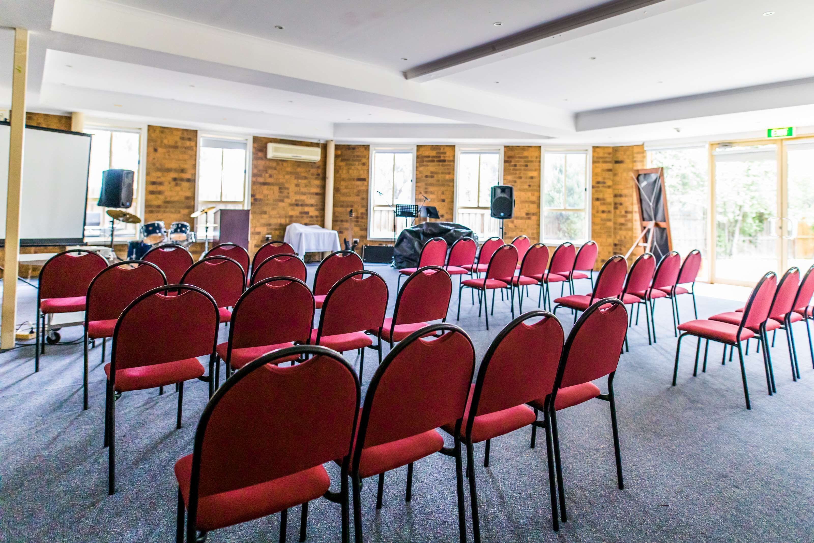 A conference room with rows of red chairs, a whiteboard, and a piano.