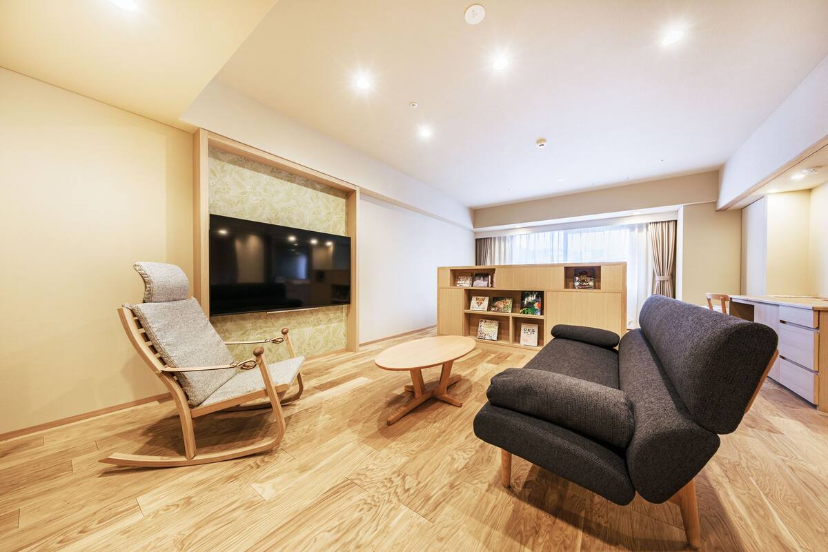 A modern living room with a wooden rocking chair, a gray sofa, a small round table, and a TV mounted on the wall.