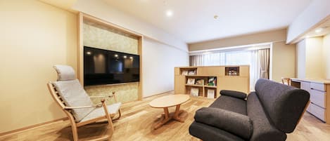 Uma sala de estar moderna com uma cadeira de balanço de madeira, um sofá cinza, uma mesa redonda pequena e uma TV fixada na parede.