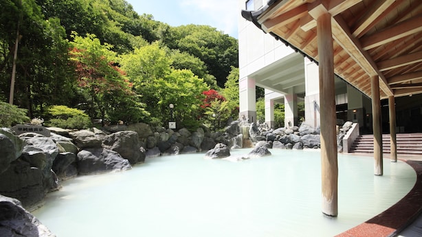 A traditional Japanese onsen with a stone bath surrounded by rocks and lush greenery. - Hotel Mahoroba (Noboribetsu)