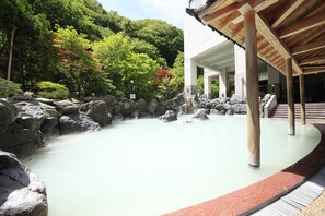 A traditional Japanese onsen with a stone bath surrounded by rocks and lush greenery. - Hotel Mahoroba (Noboribetsu)