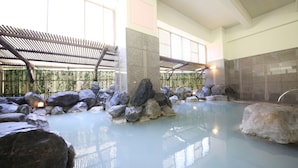 An indoor pool area with large rocks, a covered seating area, and a stone wall. - Hotel Mahoroba (Noboribetsu)