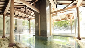 A wooden deck with a glass-enclosed pool area, stone pillars, and a view of a rocky garden. - Hotel Mahoroba (Noboribetsu)