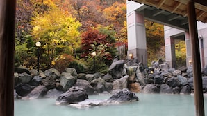 A traditional Japanese onsen with a view of autumn foliage and a stone bath area. - Hotel Mahoroba (Noboribetsu)