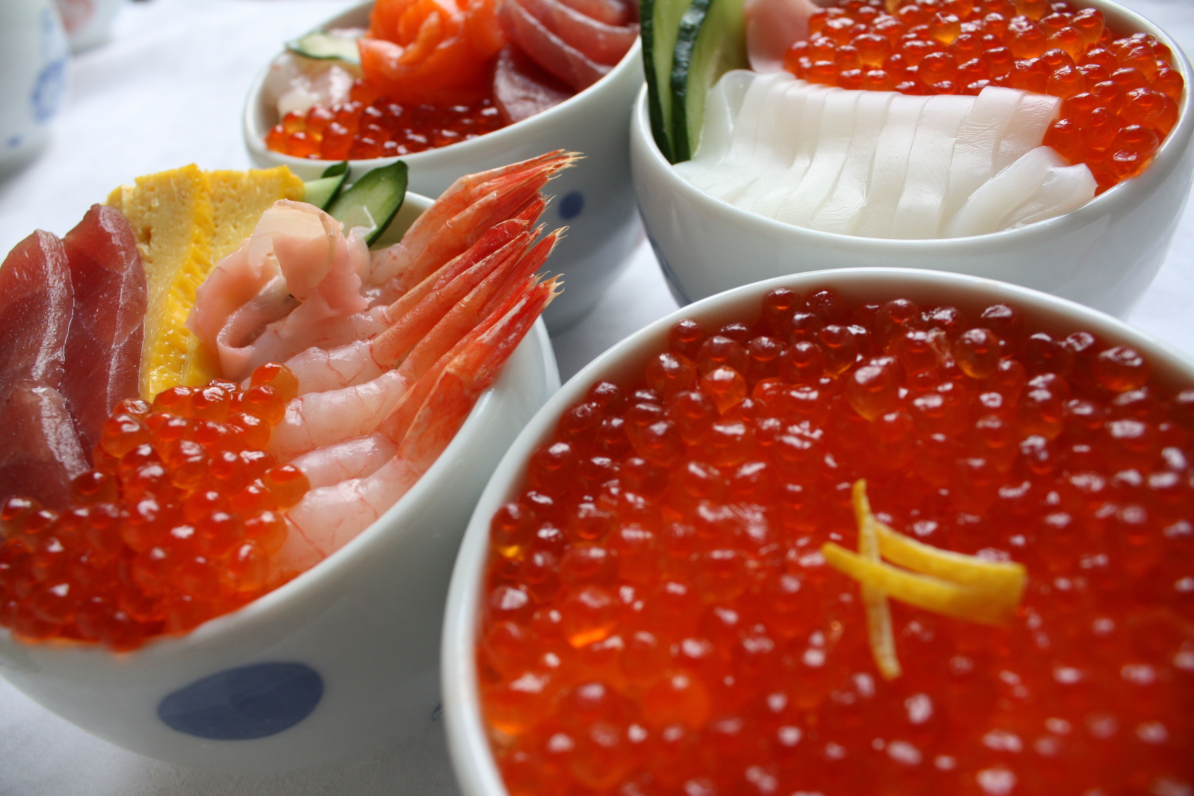 Four bowls of seafood delicacies, including shrimp, caviar, and sashimi.
