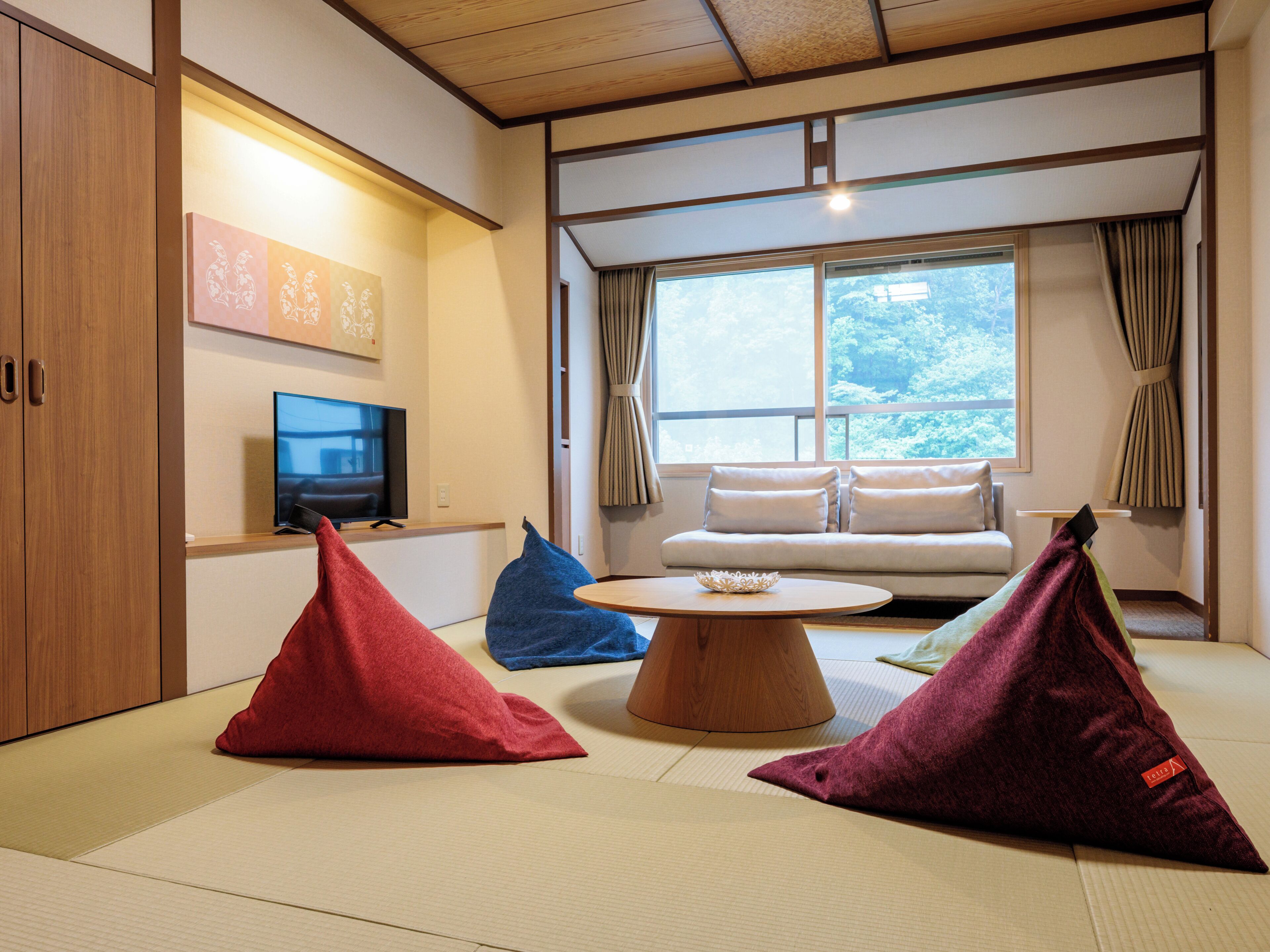 Una habitación con suelo de tatami, un sofá, un televisor y cojines.