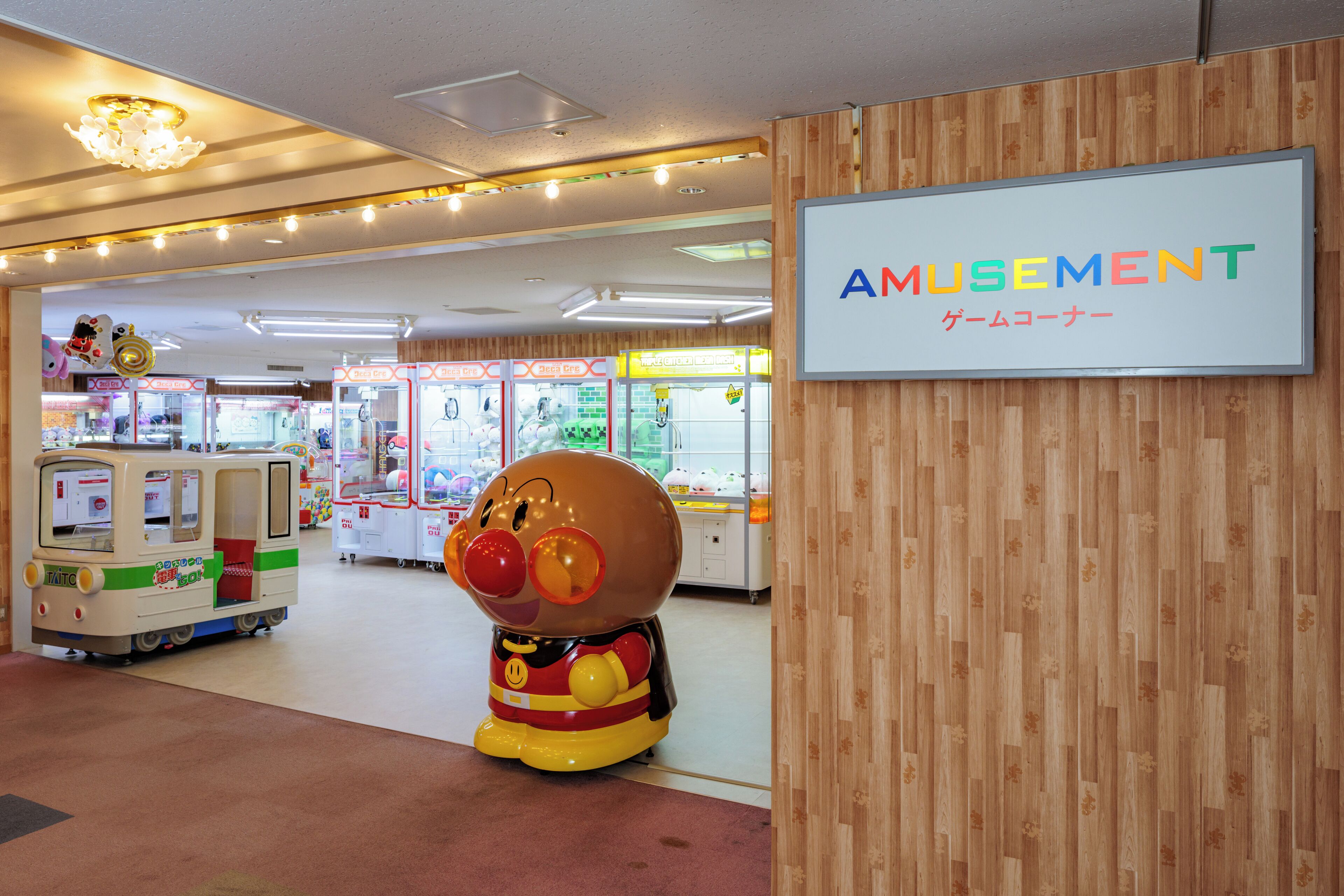 Un área de juegos interior con máquinas de garra, un peluche grande y un letrero que indica la ubicación.
