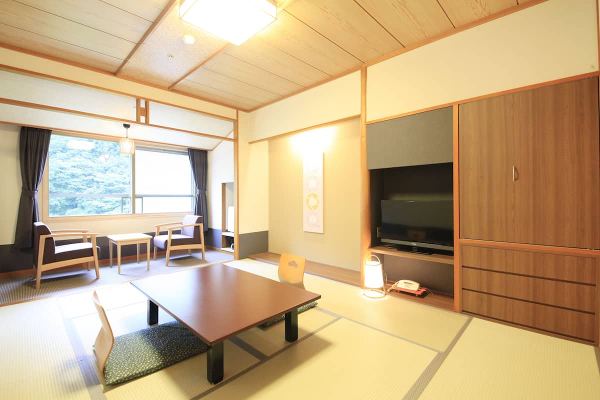 A traditional Japanese-style room with tatami flooring, a low table, seating, and a television.