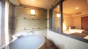 A bathroom with a large bathtub, bamboo wall panels, and a window leading to a bedroom. - Hotel Mahoroba (Noboribetsu)