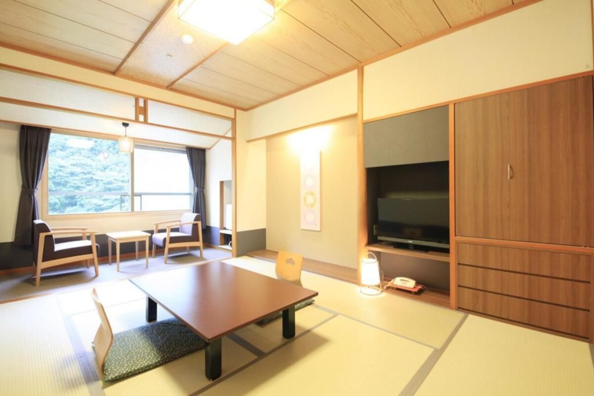 A traditional Japanese room with tatami flooring, a low table, chairs, a television, and sliding doors.