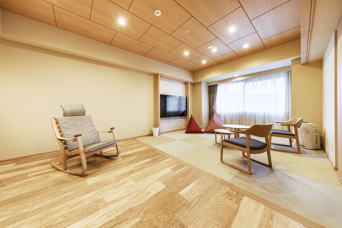 A modern room with a wooden ceiling, a TV, a sofa, a table with chairs, and a window with curtains.