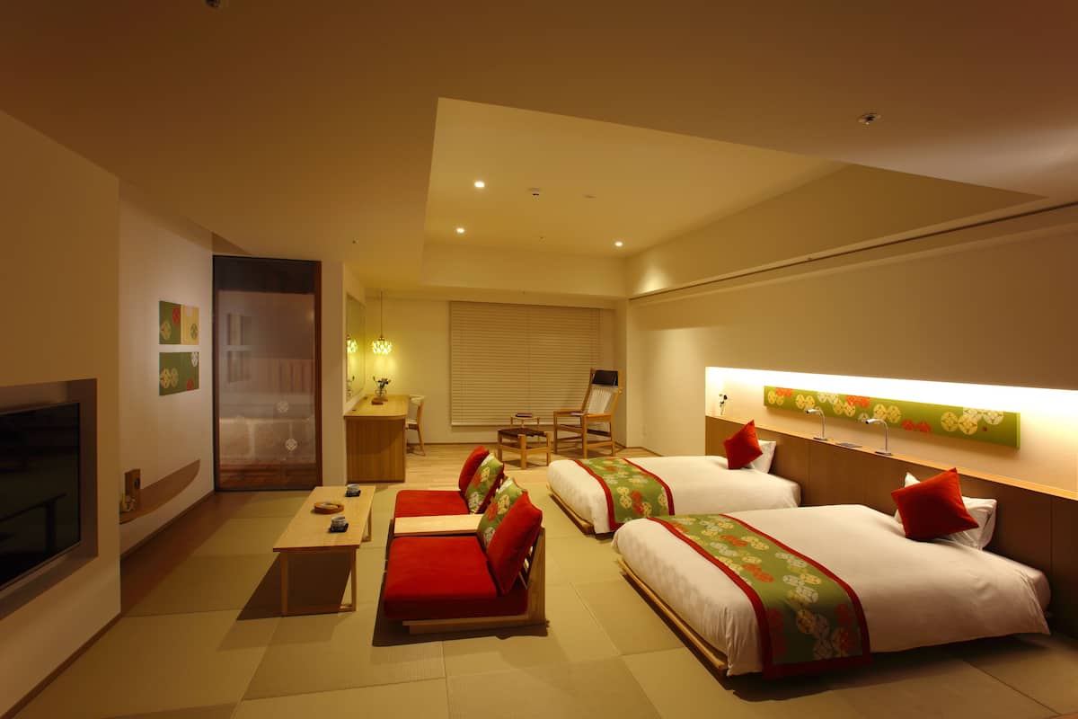 A hotel room with two beds, a sofa, a desk, and a TV.