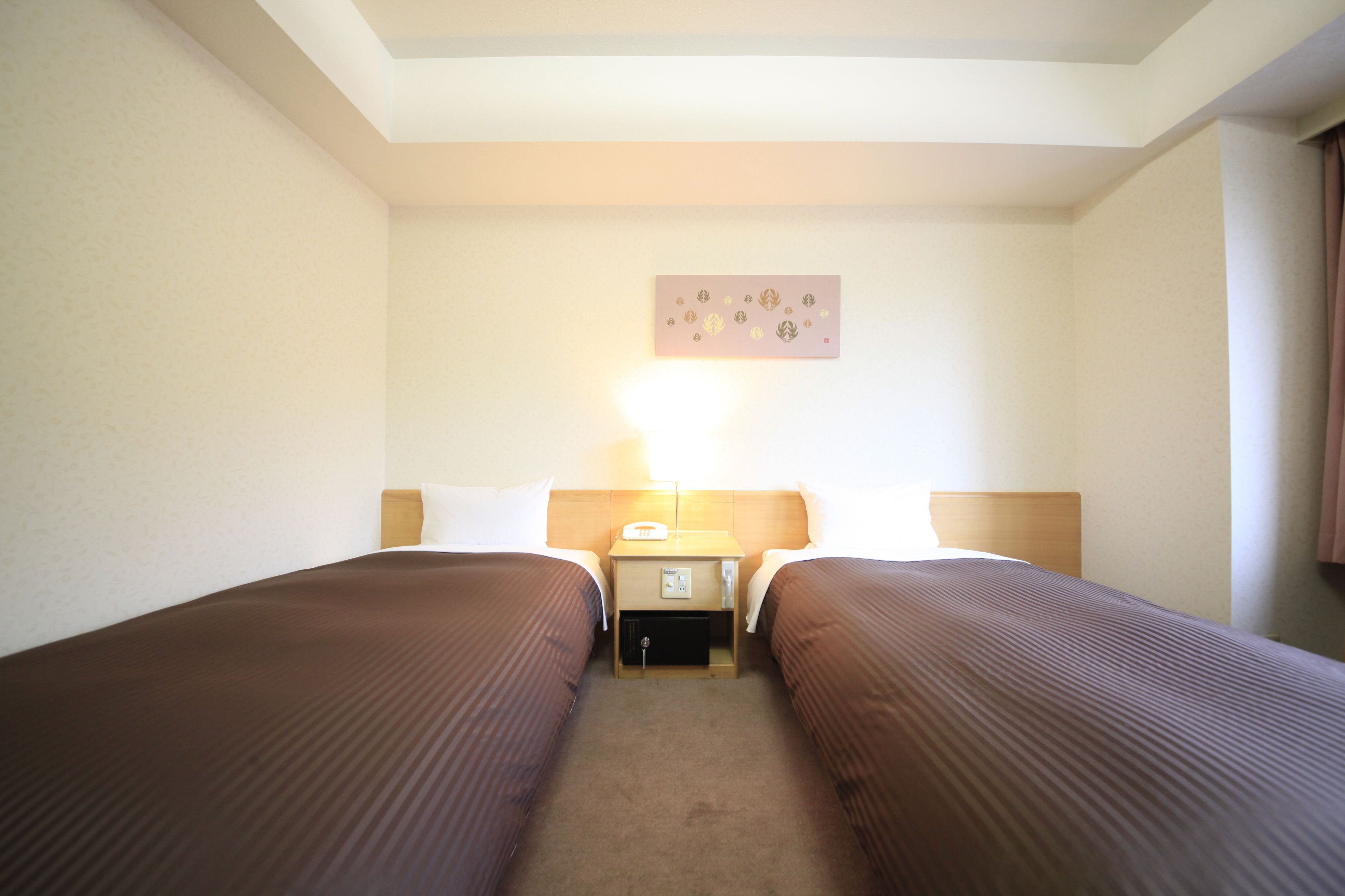 A hotel room with two single beds, a bedside table with a lamp, and a wall-mounted artwork.