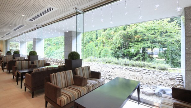 A modern indoor seating area with sofas and tables, large windows with a view of a natural landscape, and decorative string lights. - Hotel Mahoroba (Noboribetsu)