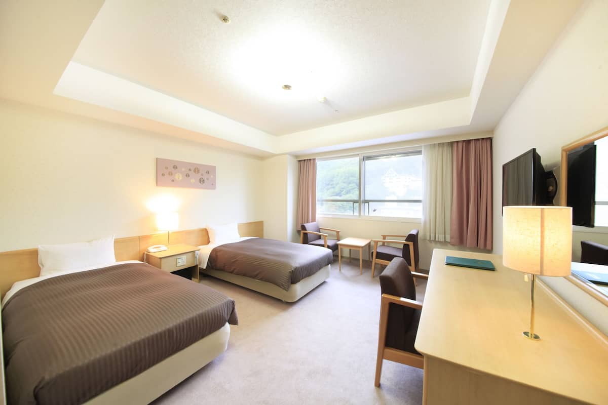 A hotel room with two beds, a desk, a chair, a lamp, and a TV.