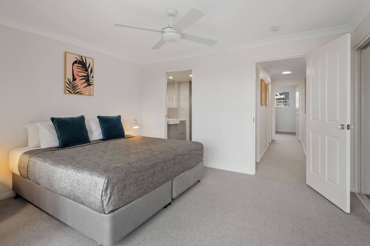 A bedroom with a bed, a ceiling fan, a door, and a hallway.