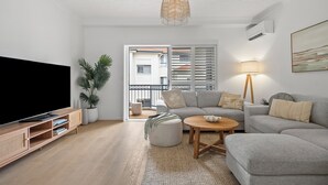 Un salon comprenant un téléviseur, un canapé, un pouf, une table basse et un luminaire suspendu.