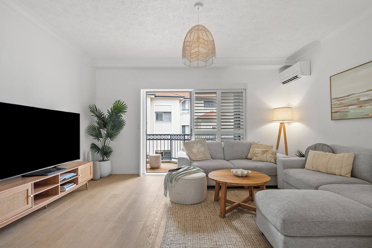 A living room with a TV, sofa, ottoman, coffee table, and a hanging light fixture.